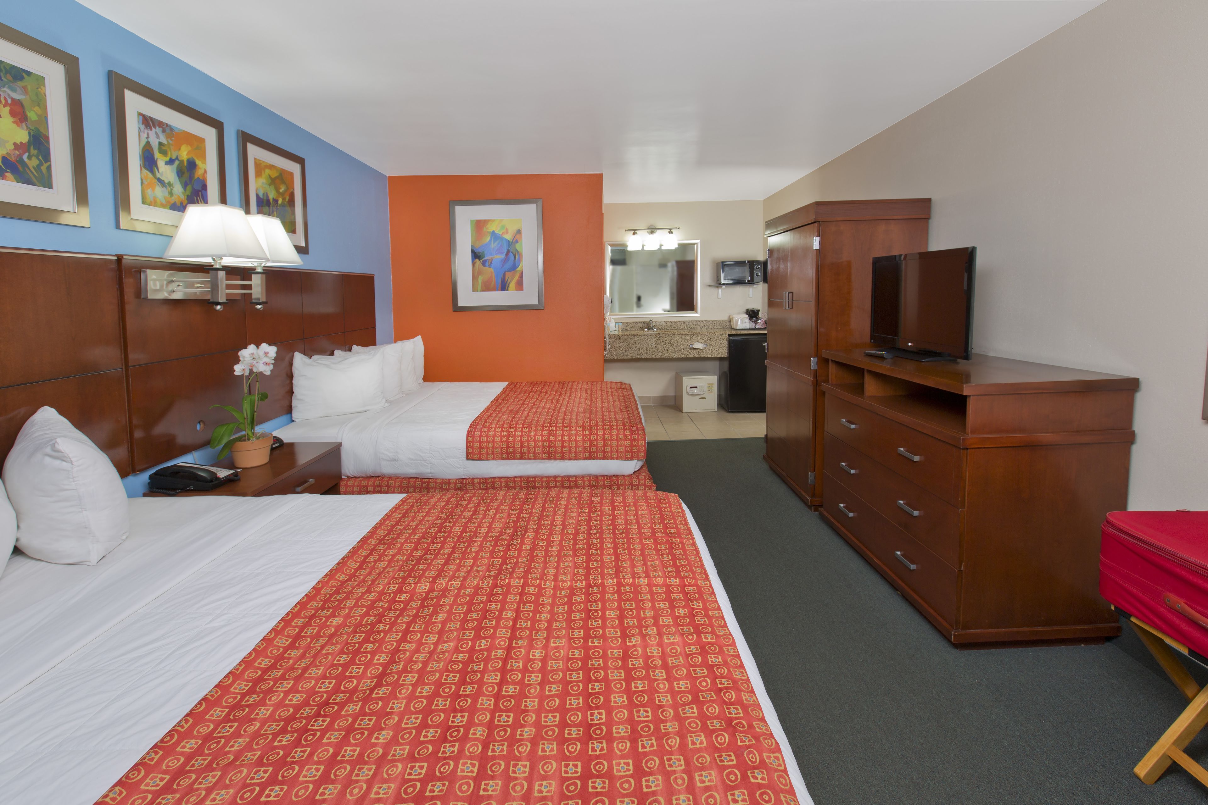 A hotel room with two beds, a TV, a dresser, and a bathroom visible in the background.