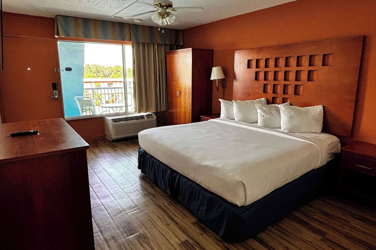 Een hotelkamer met een groot bed, een bureau, een stoel en een balkon met uitzicht.