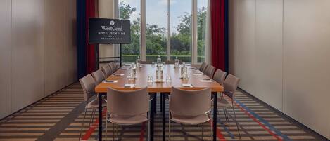 Un salón de conferencias con una mesa larga, sillas y una pantalla grande que muestra el nombre del hotel.