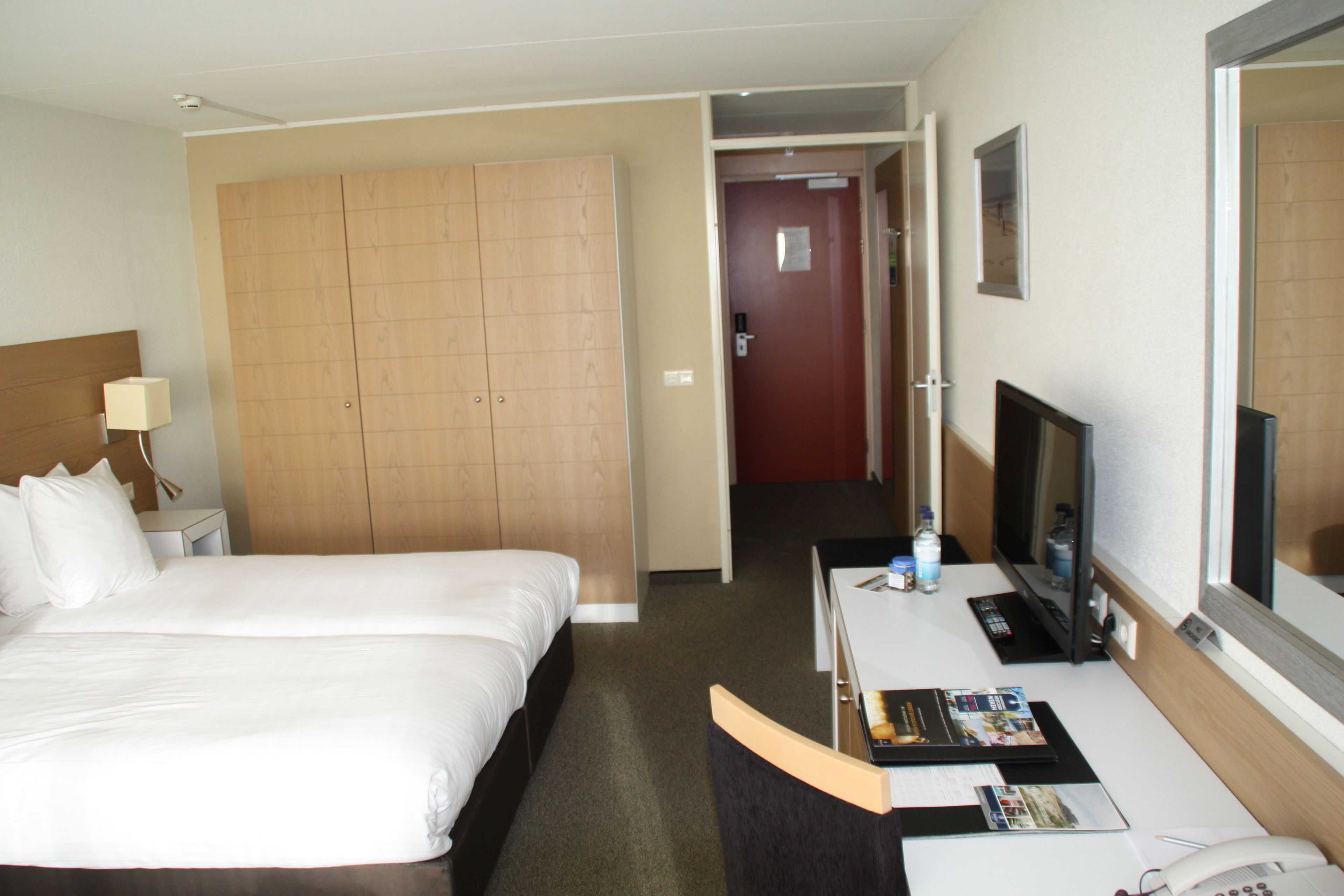 A hotel room with a large bed, a desk with a computer, a TV, and a wardrobe.