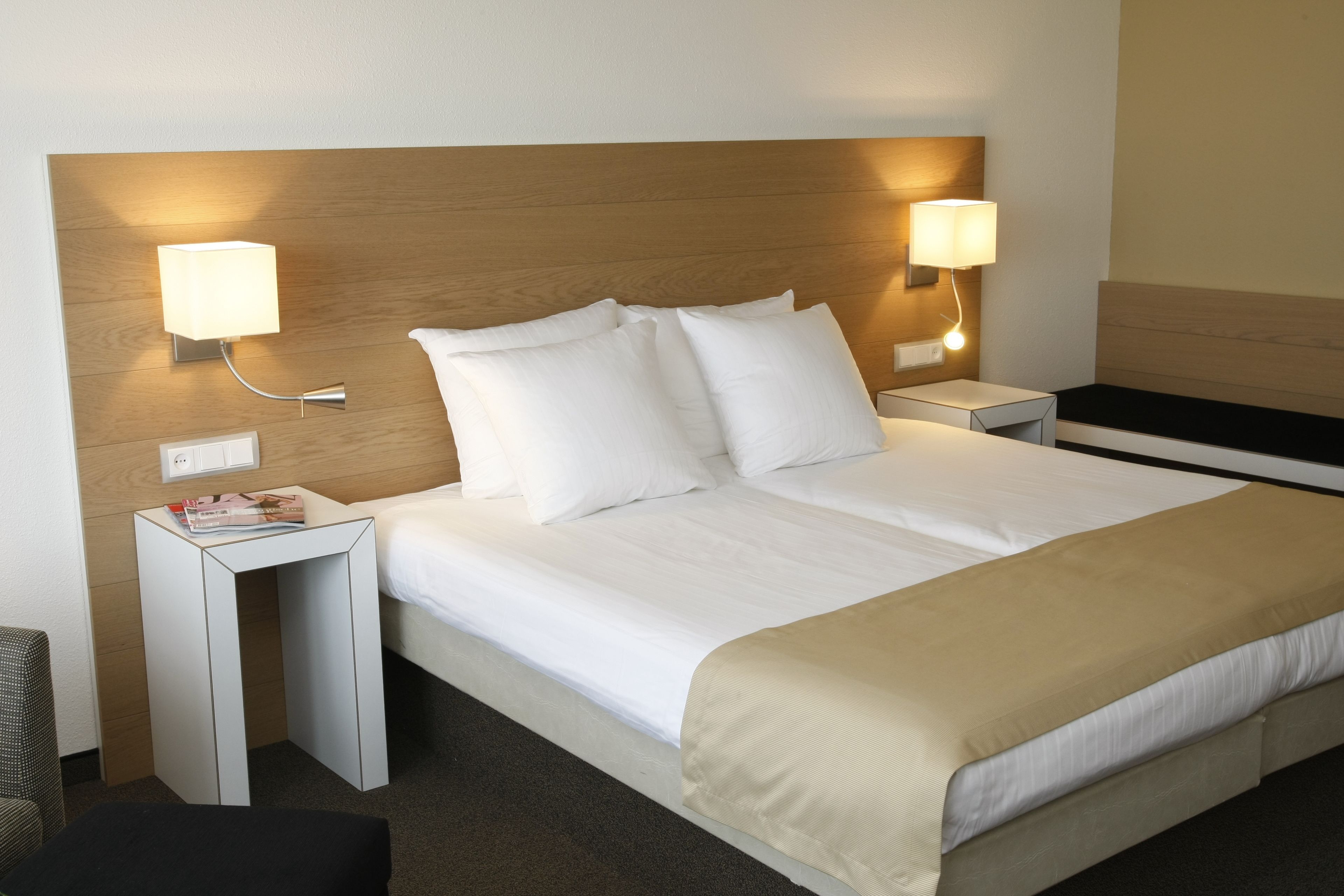 Een hotelkamer met een groot bed, twee nachtkastjes, een tijdschrift en twee wandlampen.