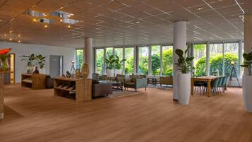 A spacious indoor area with large windows, wooden flooring, and modern furniture.