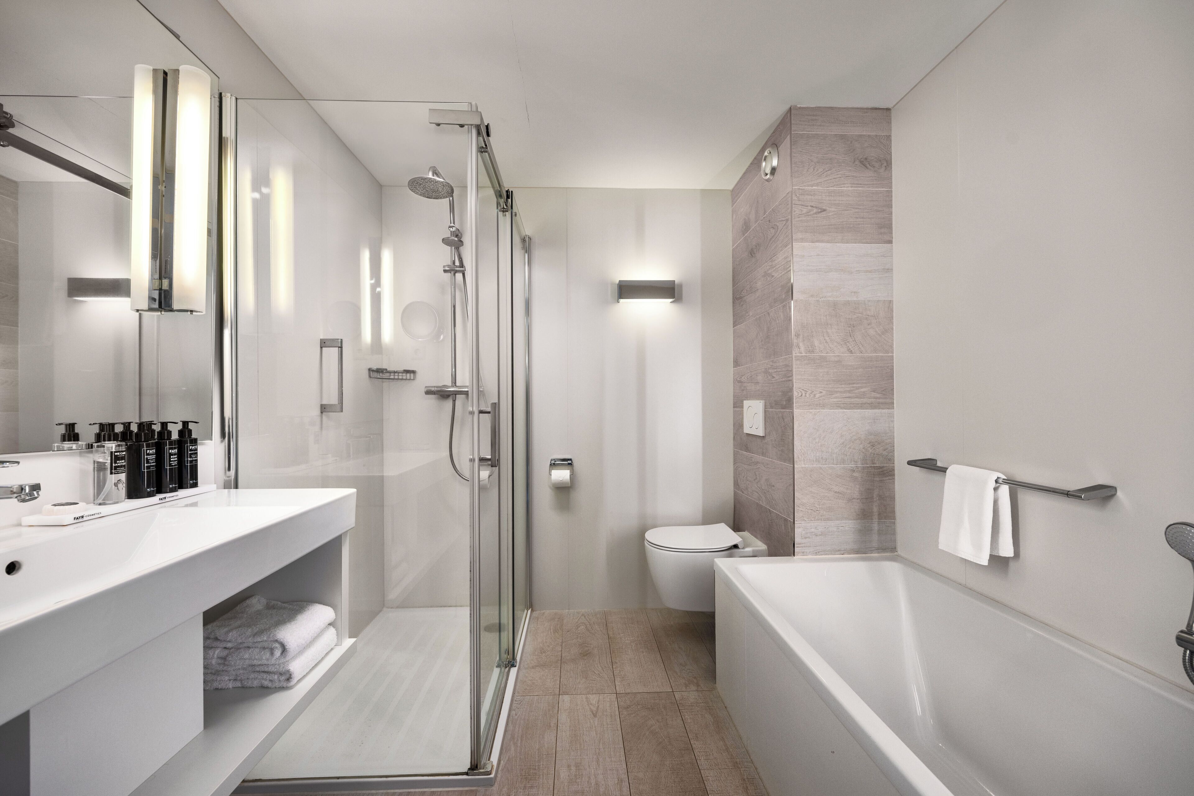 A modern bathroom with a glass-enclosed shower, a white sink with toiletries, a toilet, and a bathtub.