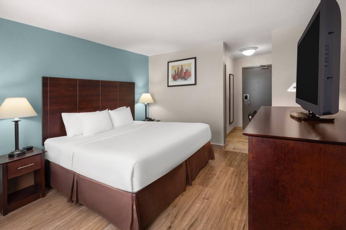 A hotel room with a bed, bedside tables, a TV, a desk, and a door.
