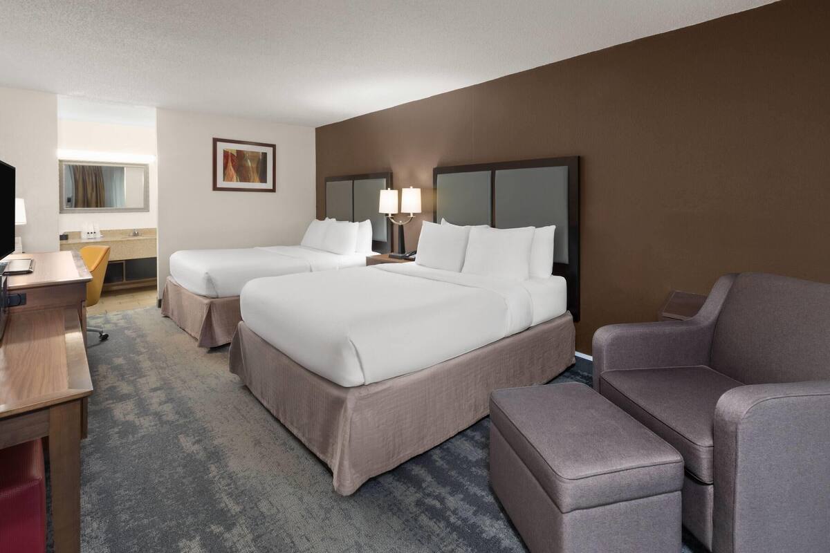 A hotel room with two beds, a desk, a chair, and a sofa.