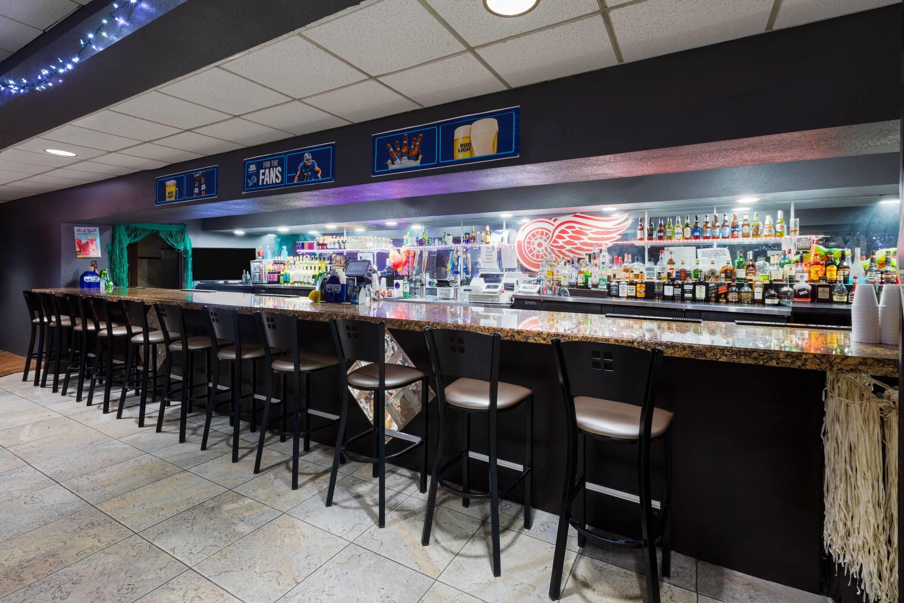 A bar area with a long counter, multiple stools, and a variety of bottles and glasses.