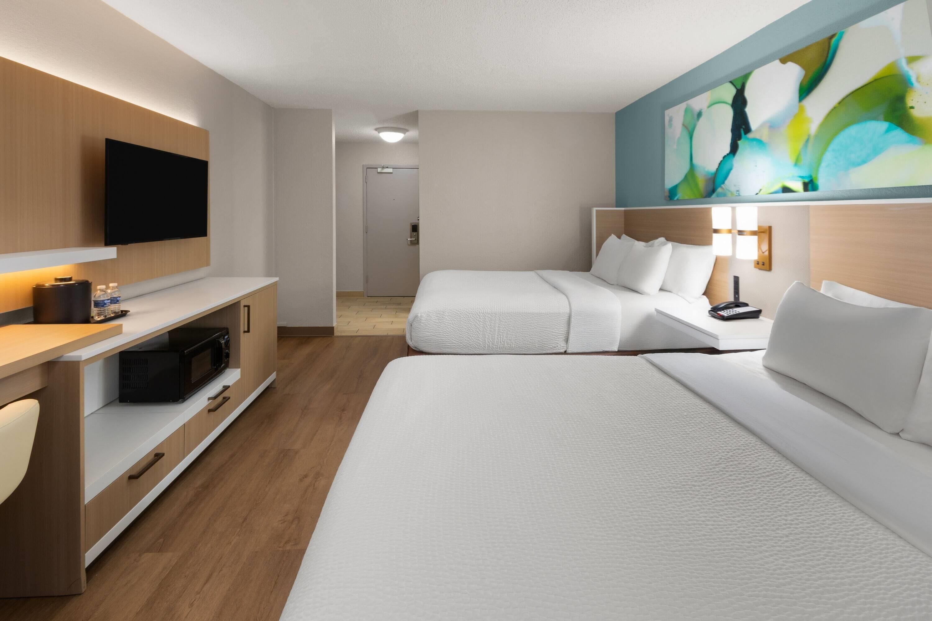 A hotel room with a bed, a TV, a desk with a microwave, and a painting on the wall.