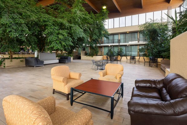 An indoor lounge area with seating arrangements, large windows, and indoor plants. - Wyndham Garden Romulus Detroit Metro Airport (Romulus)