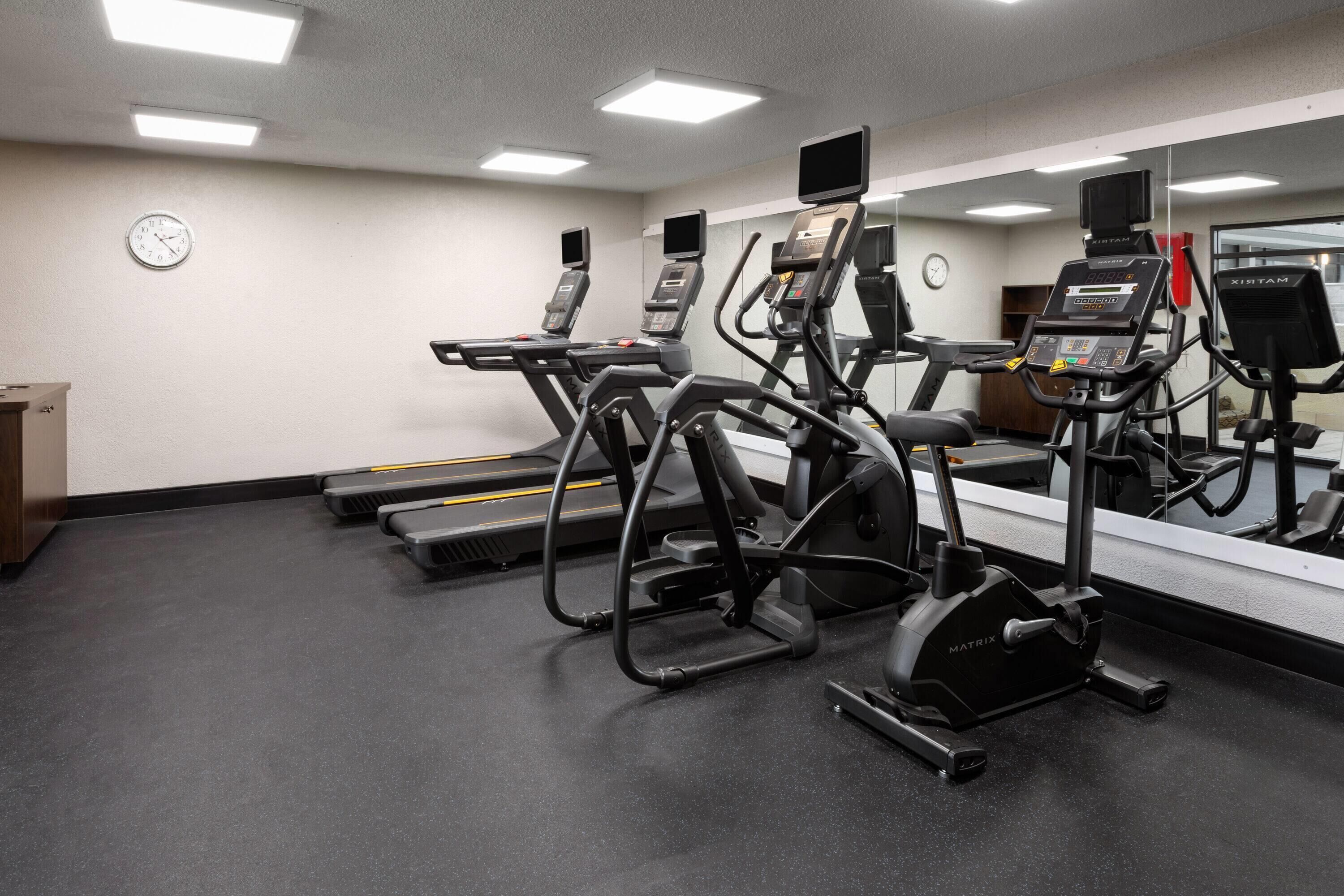 A gym with treadmills, ellipticals, and a mirrored wall.