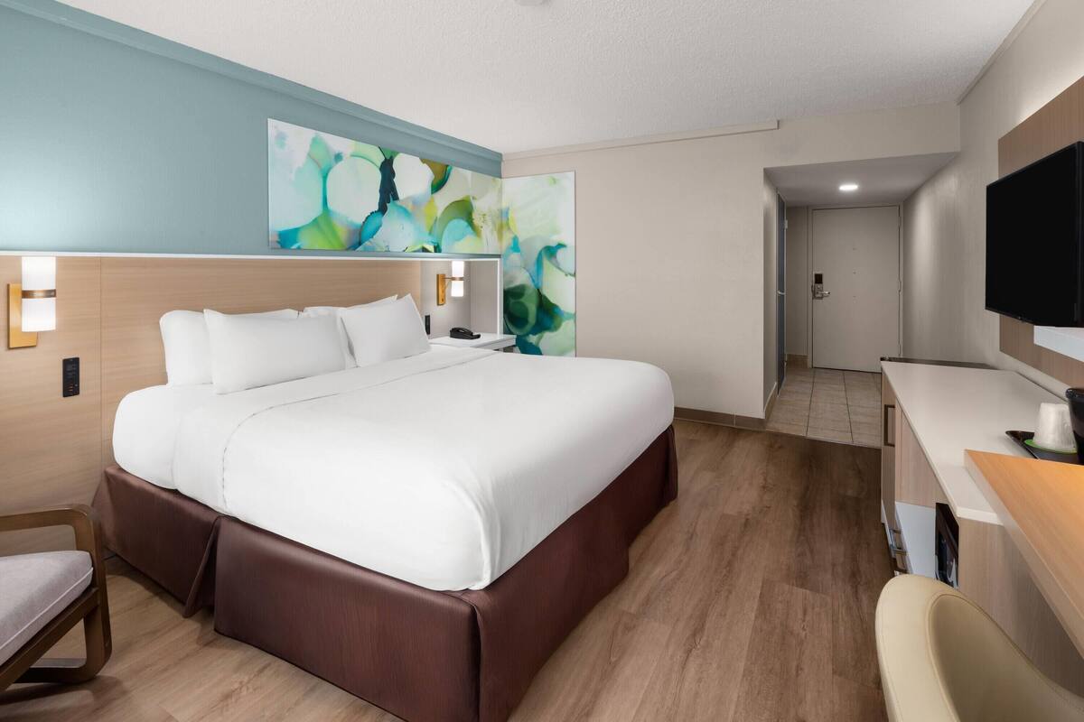 A hotel room with a large bed, a desk, a television, and a painting on the wall.