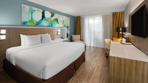 A hotel room with a large bed, a desk, a chair, a TV, and a painting on the wall.