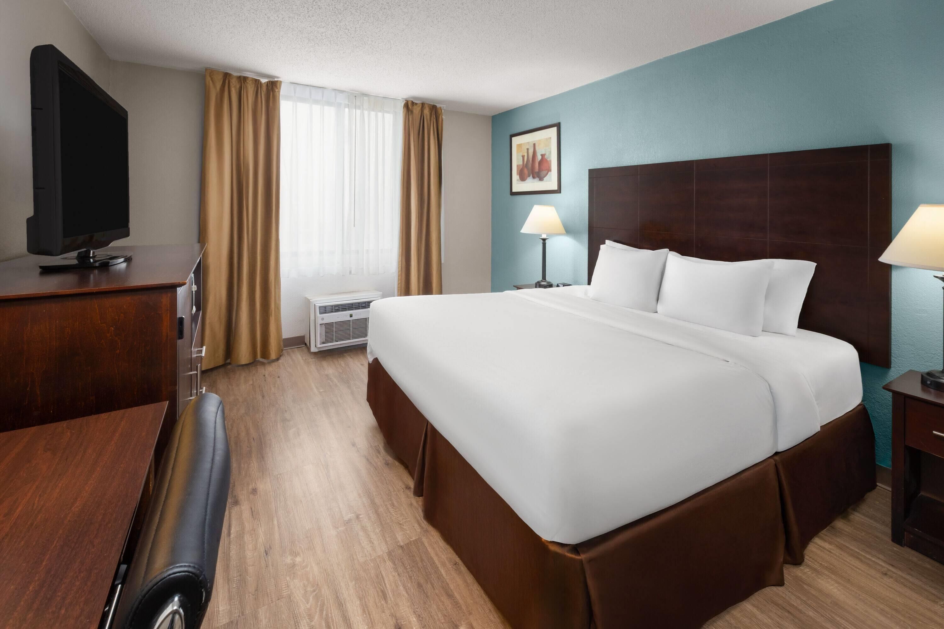 A hotel room with a large bed, a flat-screen TV, a desk, and a window with curtains.