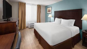 A hotel room with a large bed, a flat-screen TV, a desk, and a window with curtains.