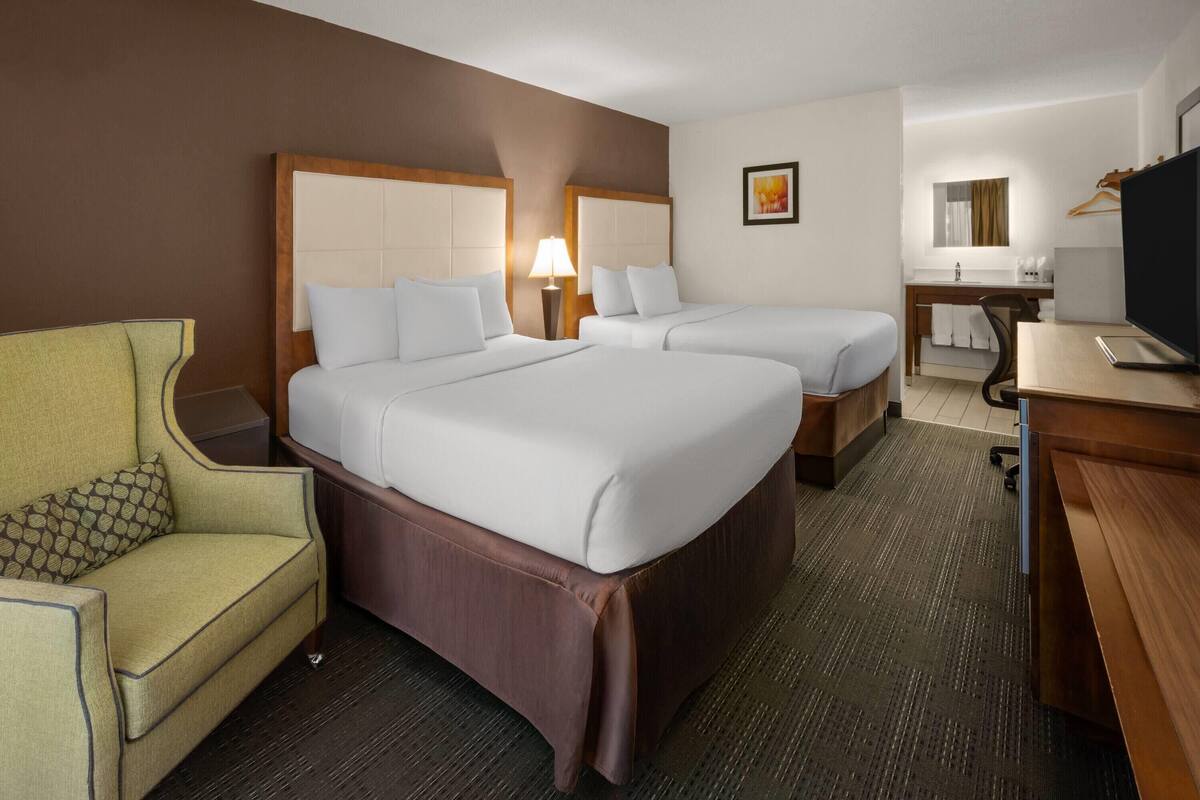 A hotel room with two beds, a desk, a chair, a TV, and a bathroom visible in the background.