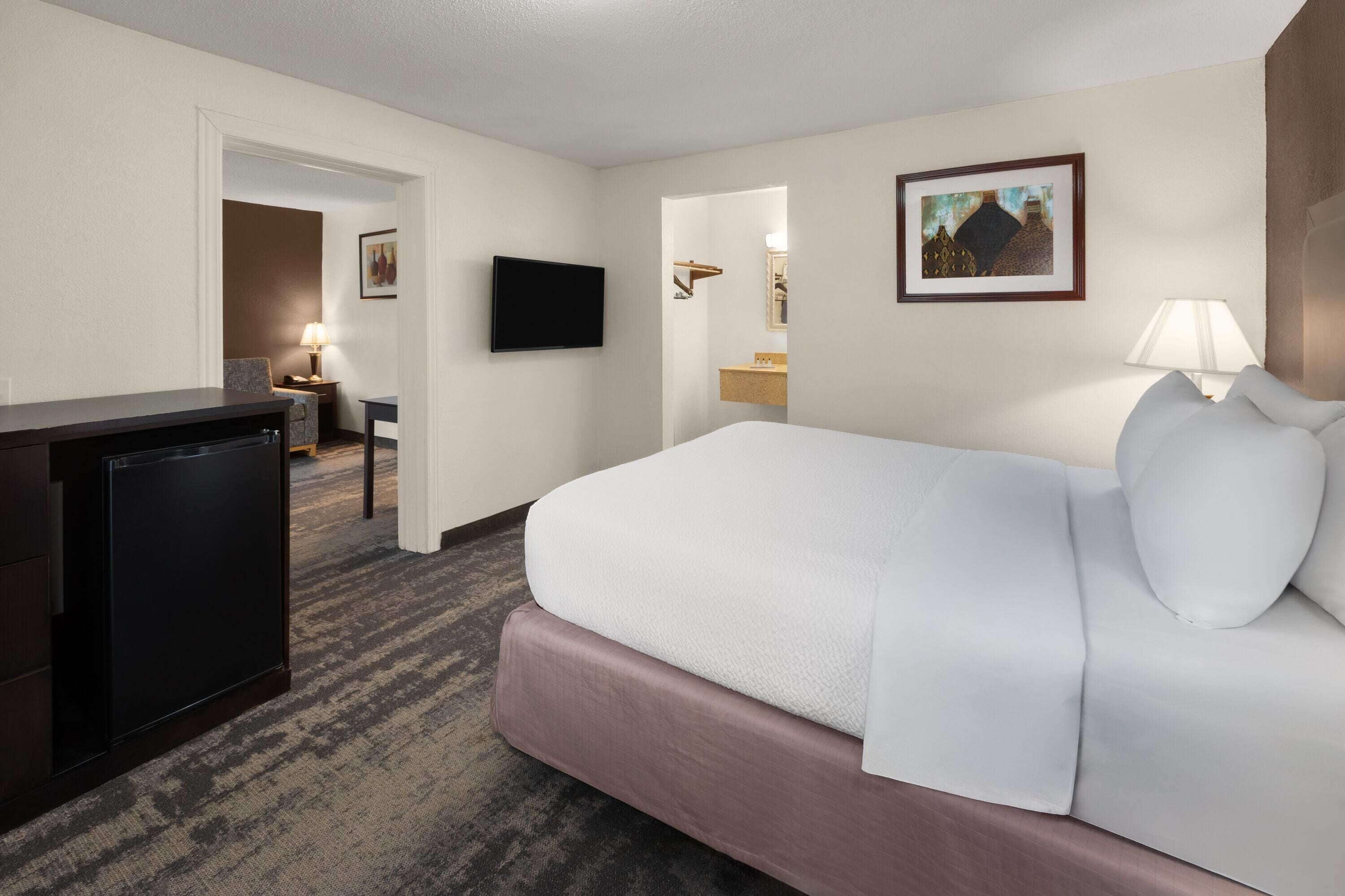 Una habitación de hotel con una cama, televisión, escritorio y lámpara.