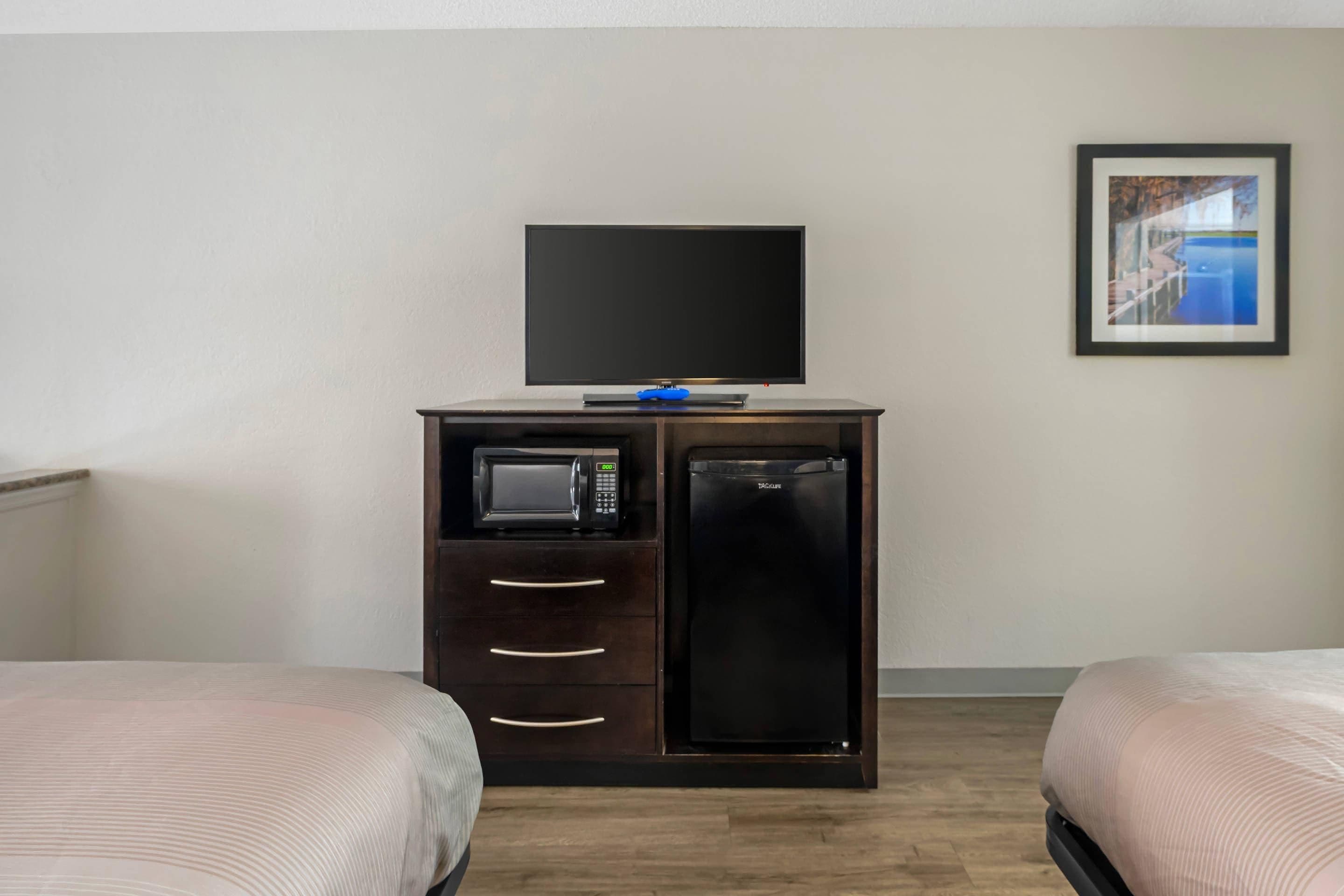 A hotel room with a bed, a TV on a cabinet, a microwave, and a refrigerator.