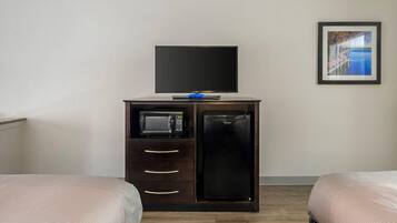 A hotel room with a bed, a TV on a cabinet, a microwave, and a refrigerator.