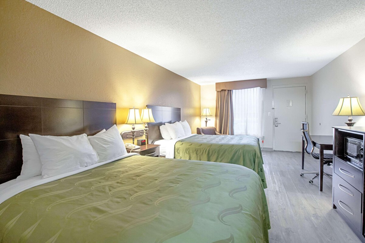 Habitación de hotel con dos camas, un escritorio, una silla y un televisor.