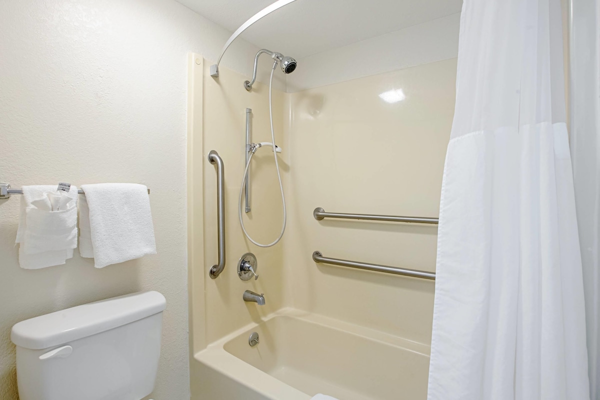 A bathroom with a toilet, a bathtub, and a shower with grab bars.