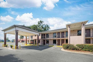 A motel with a covered parking area, multiple rooms, and a gas station in the background. - Quality Inn & Suites Live Oak I-10 Exit 283 (Live Oak)