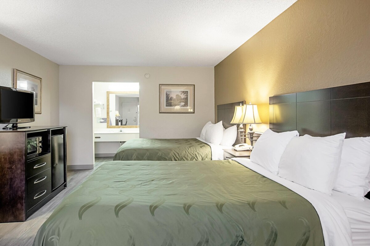 A hotel room with two beds, a TV, a desk with drawers, a mirror, and a lamp.
