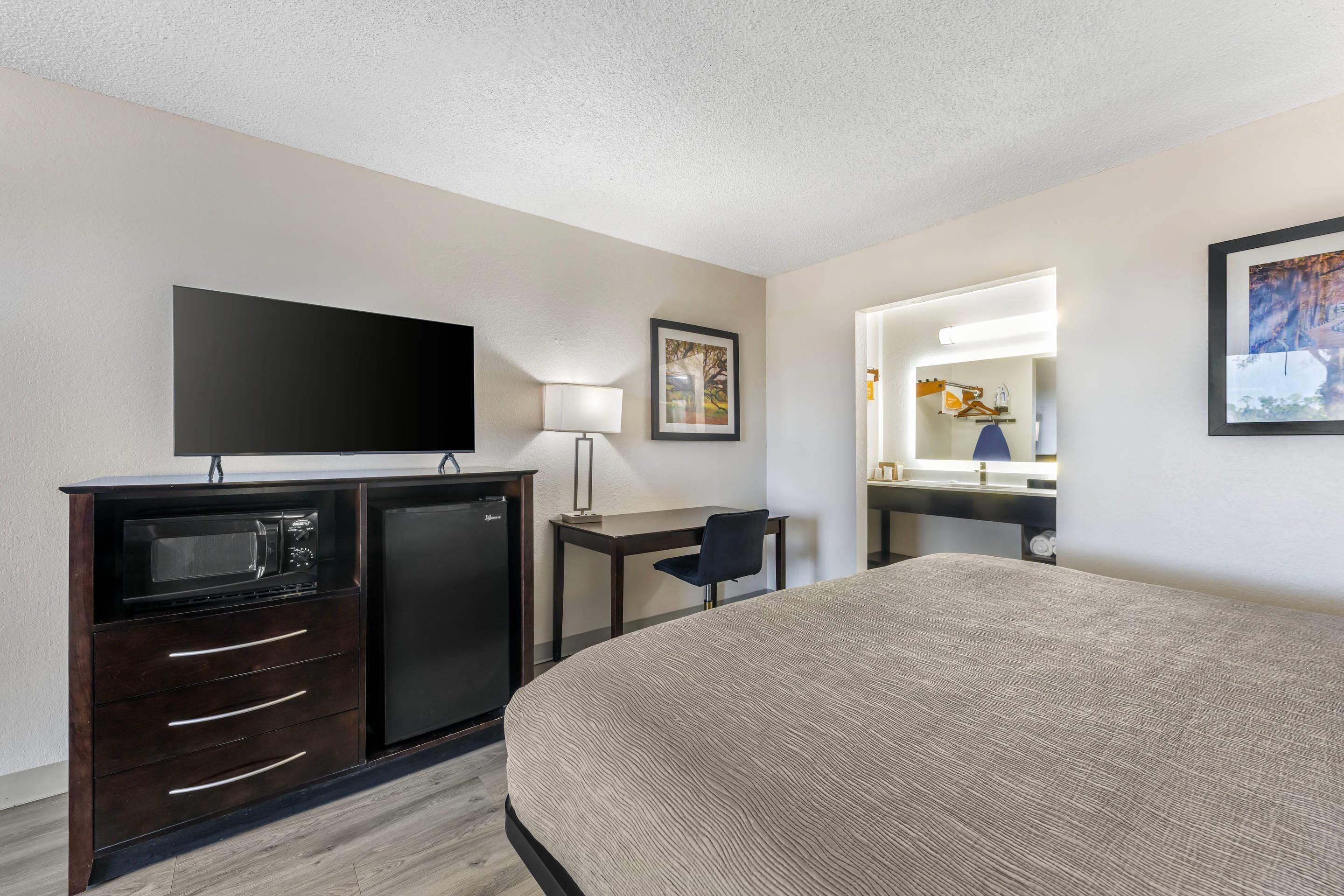 A hotel room with a bed, a desk, a television, a refrigerator, a microwave, a chair, and a mirror.