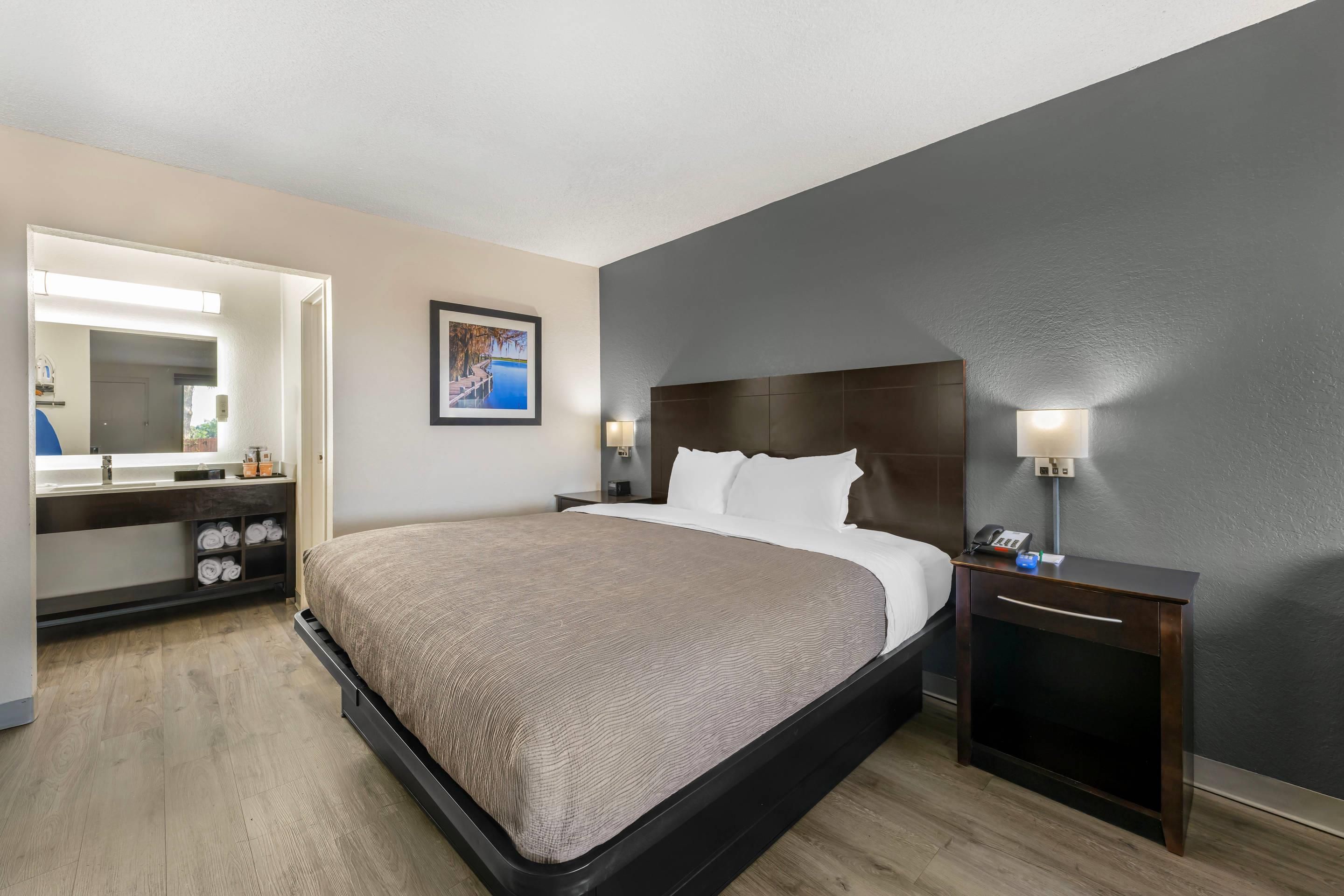 A hotel room with a bed, a bedside table, a nightstand, a mirror, and a picture on the wall.
