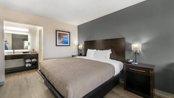 A hotel room with a bed, a bedside table, a nightstand, a mirror, and a picture on the wall.