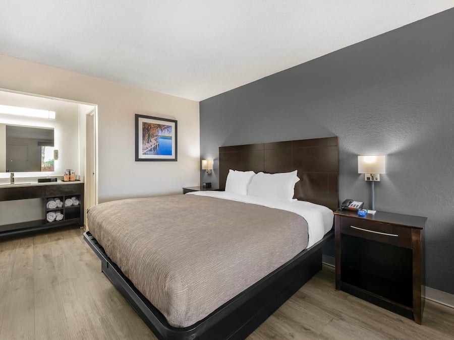 A hotel room with a bed, a bedside table, a nightstand, a mirror, and a picture on the wall.