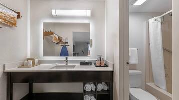 A modern bathroom with a sink, mirror, and toilet. There is a towel rack with towels and a shower curtain visible.