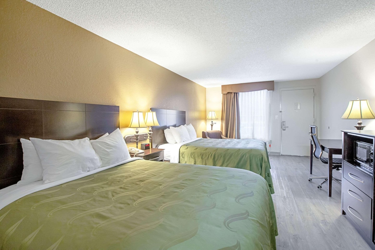 Habitación de hotel con dos camas, un escritorio, una silla y un televisor.