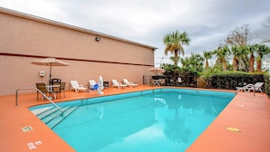 Una piscina rectangular con interior azul, rodeada por una solana anaranjada. Hay sillas de descanso y sombrillas a lo largo de la piscina.