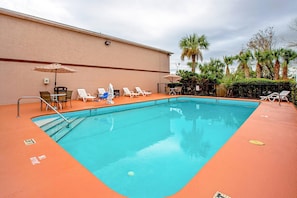A rectangular swimming pool with a blue interior, surrounded by a low orange deck. There are lounge chairs and umbrellas along the poolside. - Quality Inn & Suites Live Oak I-10 Exit 283 (Live Oak)