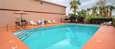 Una piscina rectangular con interior azul, rodeada por una terraza naranja baja. Hay sillas reclinables y sombrillas blancas dispuestas alrededor de la piscina.