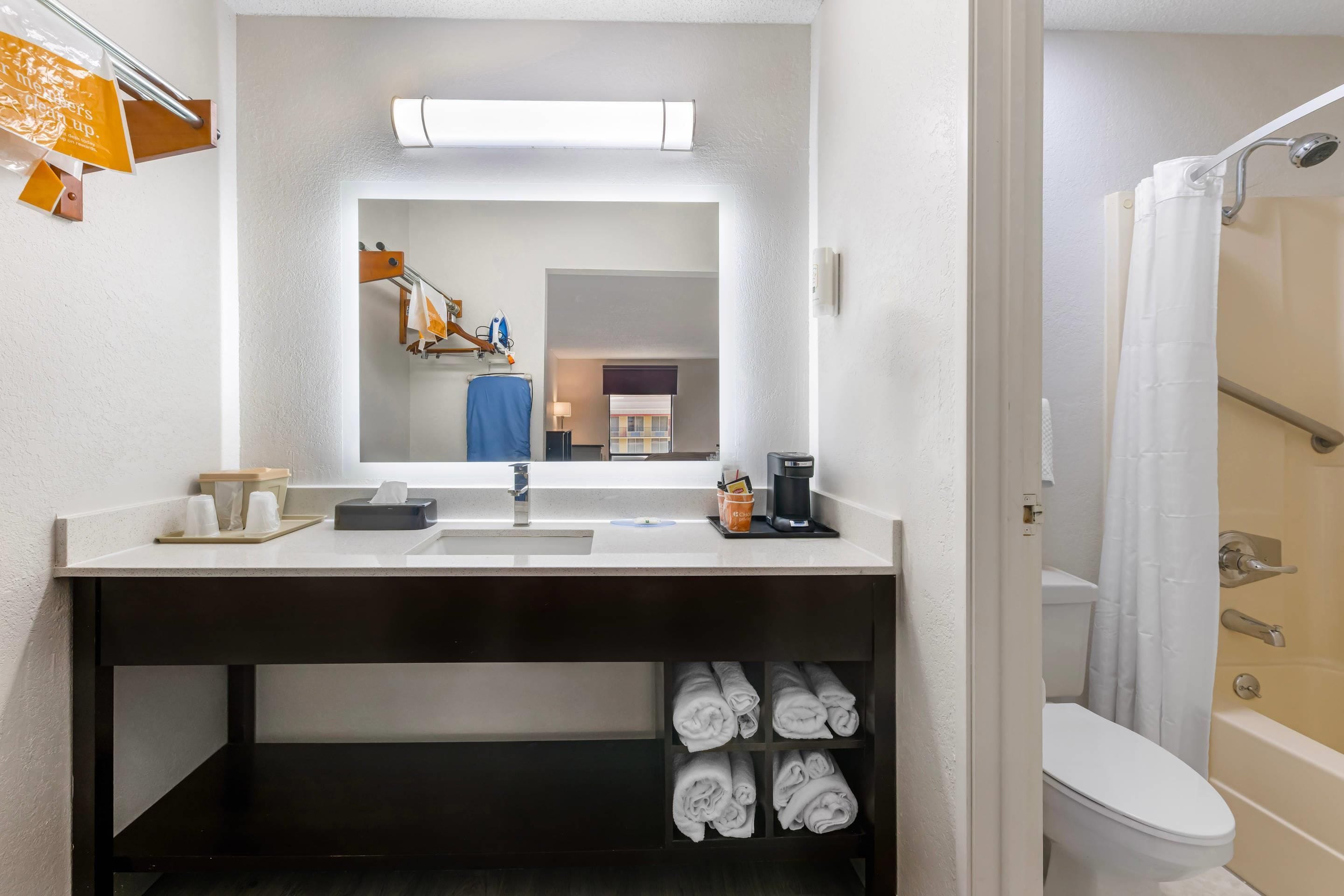A hotel bathroom with a sink, mirror, towel rack, and a shower area.