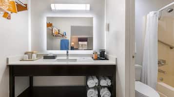 A hotel bathroom with a sink, mirror, towel rack, and a shower area.