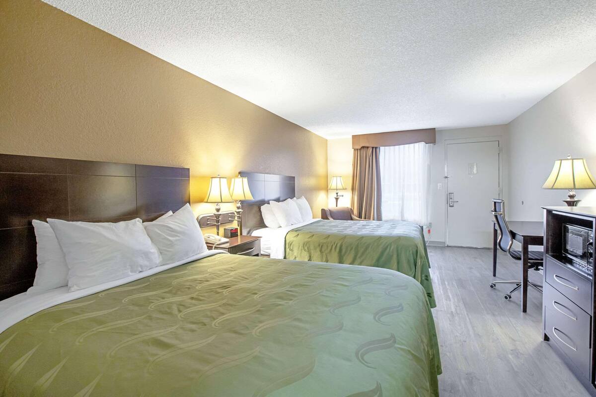 A hotel room with two beds, a desk, a chair, and a television.