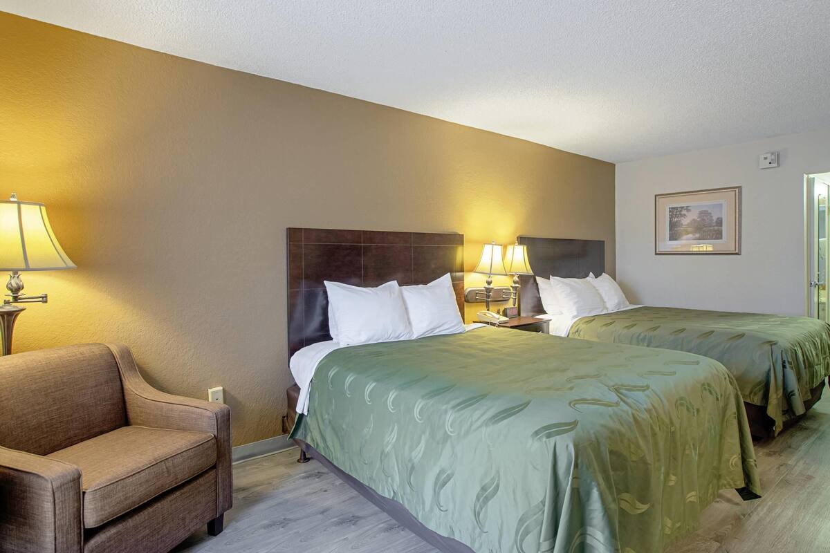 A hotel room with two beds, a sofa, bedside lamps, and a framed picture on the wall.