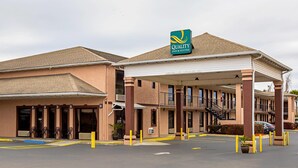 Un hôtel avec une enseigne indiquant « Quality Inn & Suites », une entrée abritée et un parking.