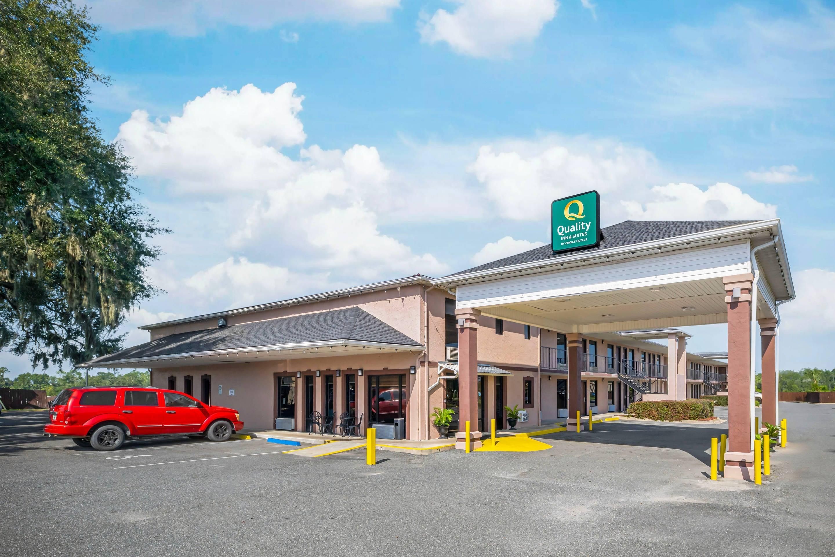 A hotel with a covered parking area, a red car parked inside, and a sign indicating it is a Quality Inn & Suites by Choice Hotels.