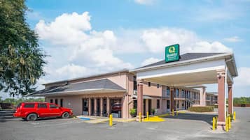 A hotel with a covered parking area, a red car parked inside, and a sign indicating it is a Quality Inn & Suites by Choice Hotels.