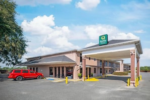A hotel with a covered parking area, a red car parked inside, and a sign indicating it is a Quality Inn & Suites by Choice Hotels.