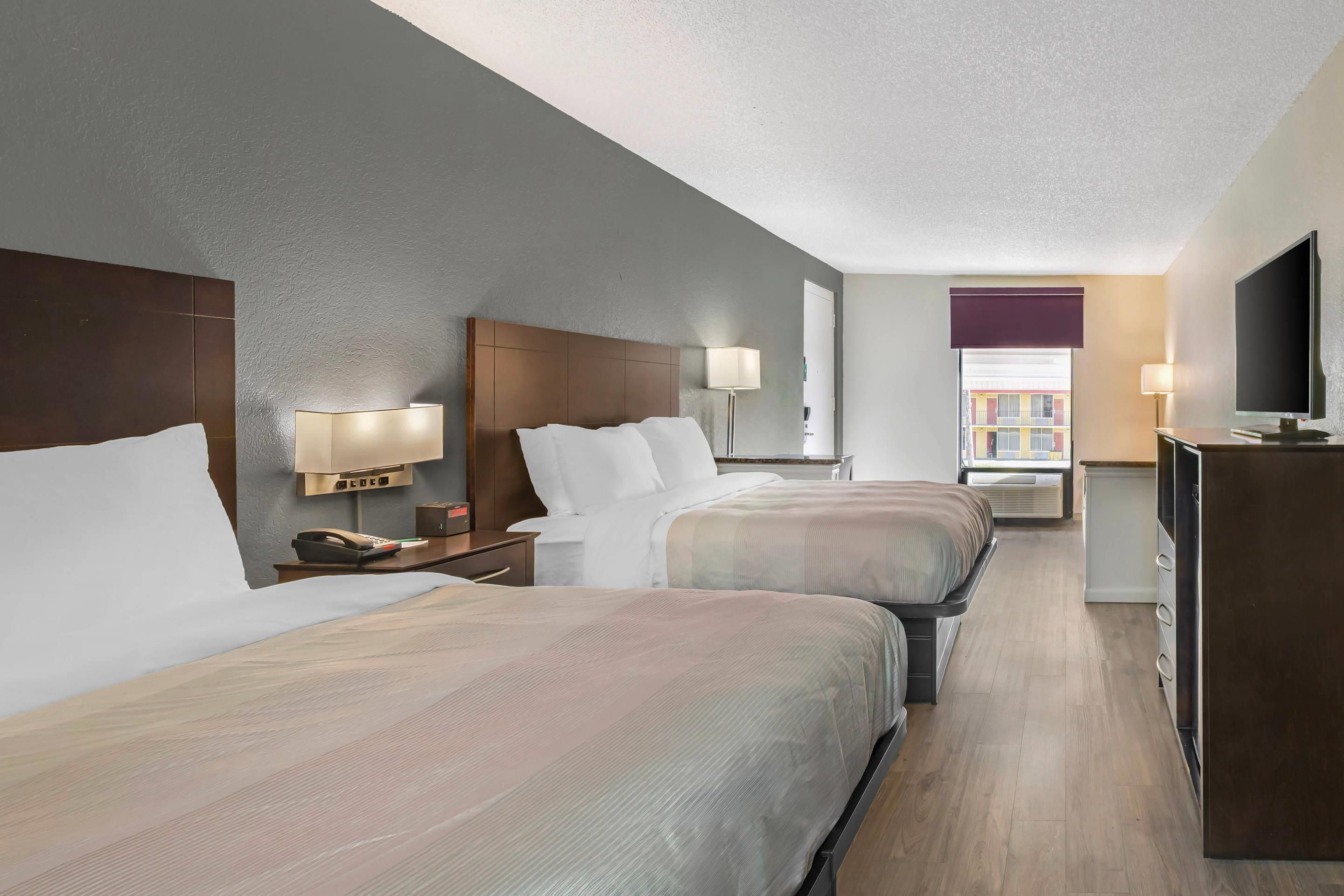 A hotel room with two beds, bedside lamps, a desk with a telephone, and a television.