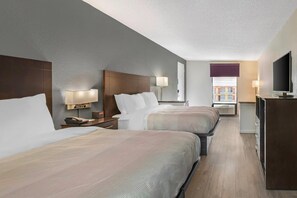 Una habitación de hotel con dos camas, lámparas de noche, un escritorio con teléfono y televisor.