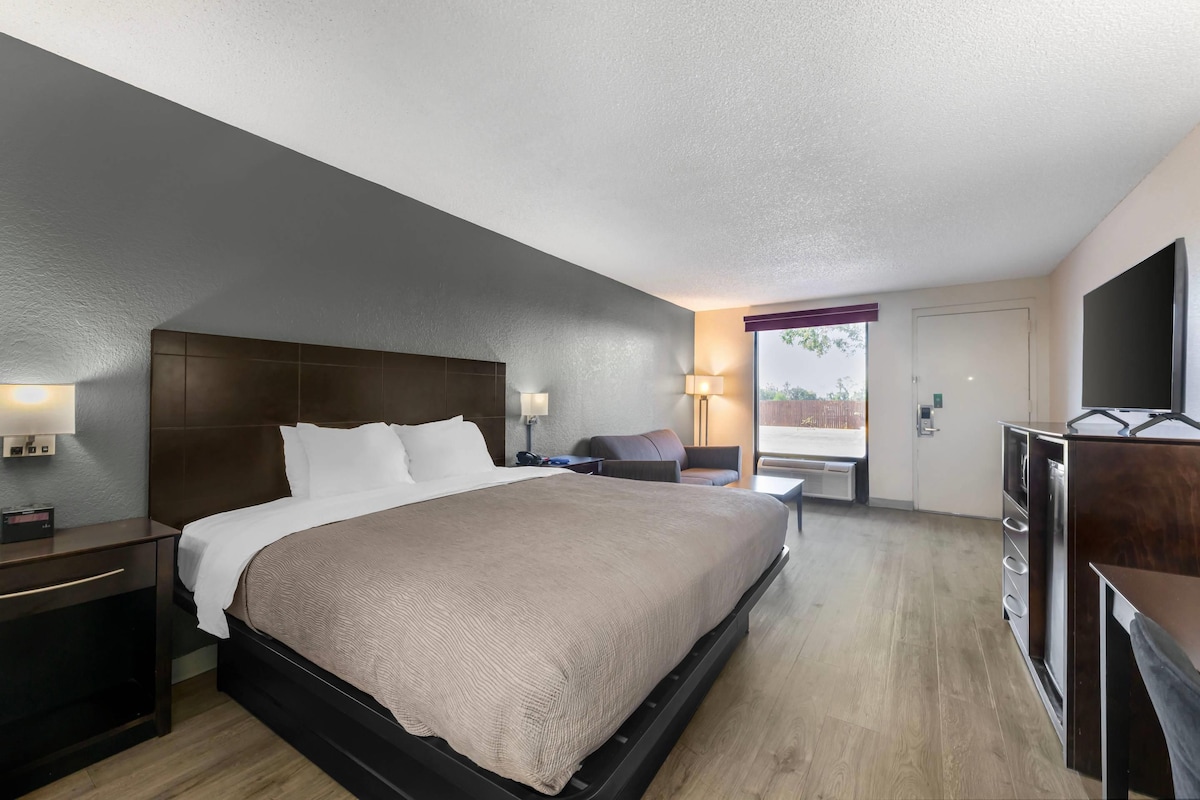 A hotel room with a large bed, bedside tables, a desk, a chair, and a TV.