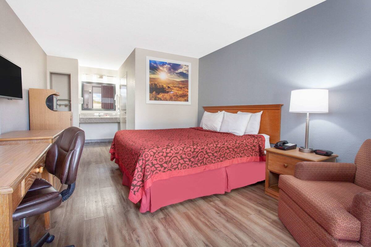 A hotel room with a bed, a desk, a chair, a nightstand, and a TV.