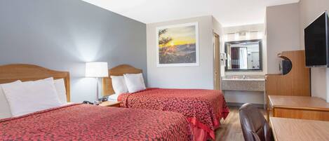 A hotel room with two beds, a desk, a chair, a TV, a bathroom mirror, and a painting of a sunset.