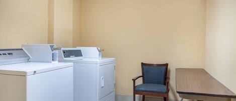 A laundry room with a washing machine, dryer, chair, and table.
