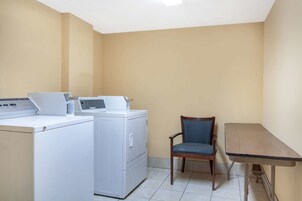 A laundry room with a washing machine, dryer, chair, and table.