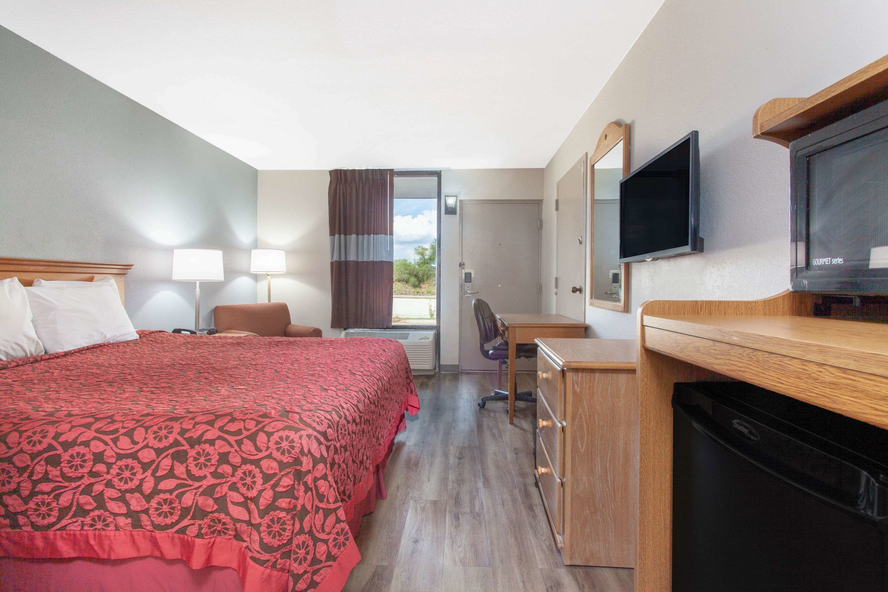 A hotel room with a bed, desk, chair, television, and a window with curtains.